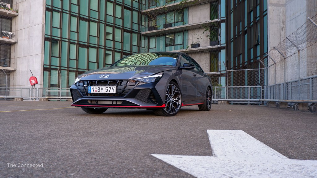 Hyundai i30 Sedan N front view at urban rooftop carpark in front of road-painted arrow