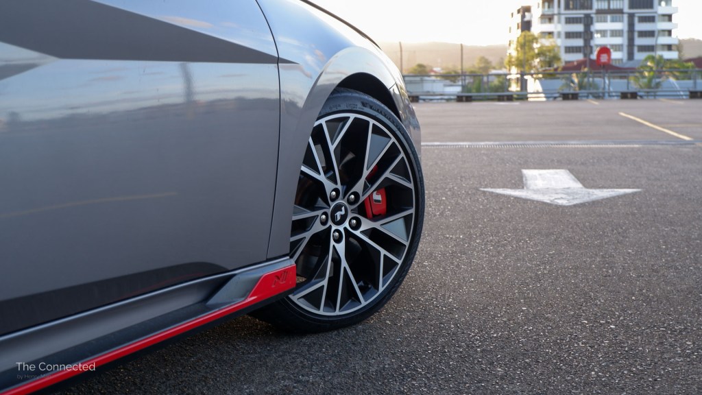 Hyundai i30 Sedan N alloy wheel with red brake calliper and side skirt at urban rooftop car park