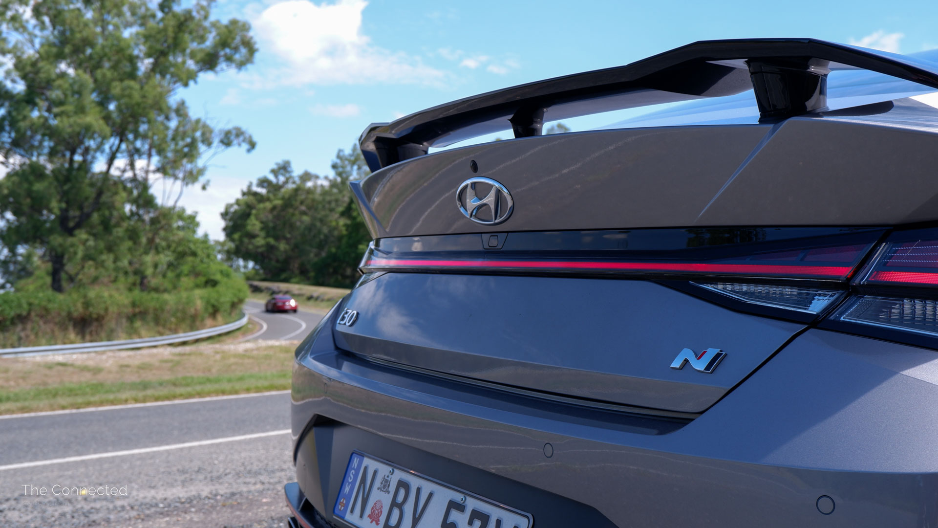 Hyundai i30 Sedan N rear LED light bar with Ford Mustang driving past mountain road