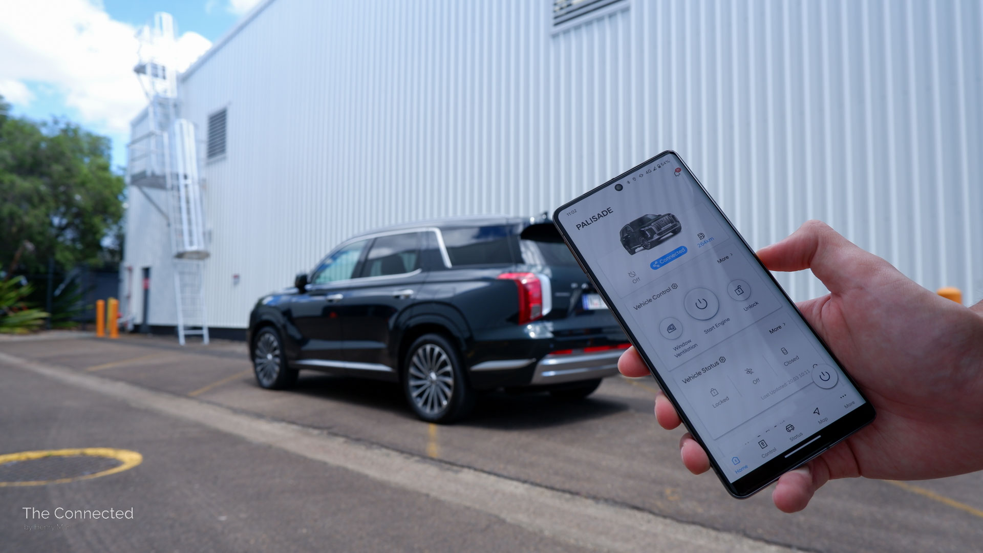 Hyundai Blulink app on smartphone in front of Hyundai Palisade Highlander