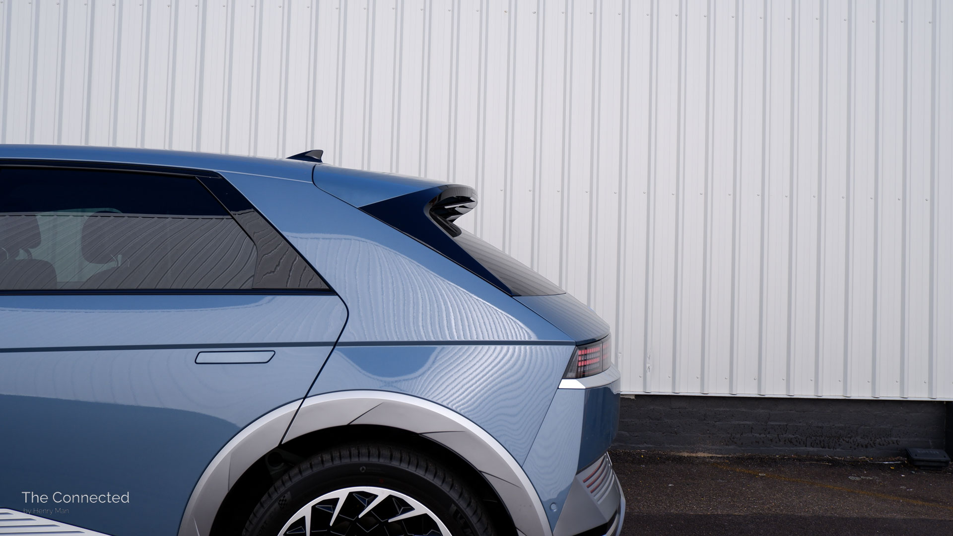 Blue Hyundai Ioniq 5 rear C-pillar in front of white corten steel