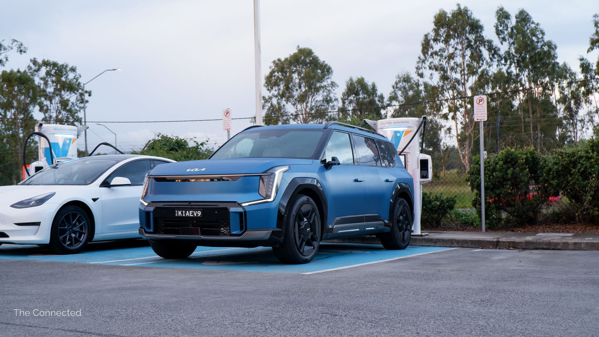 Kia EV9 at public EV charging station next to white Tesla Model 3