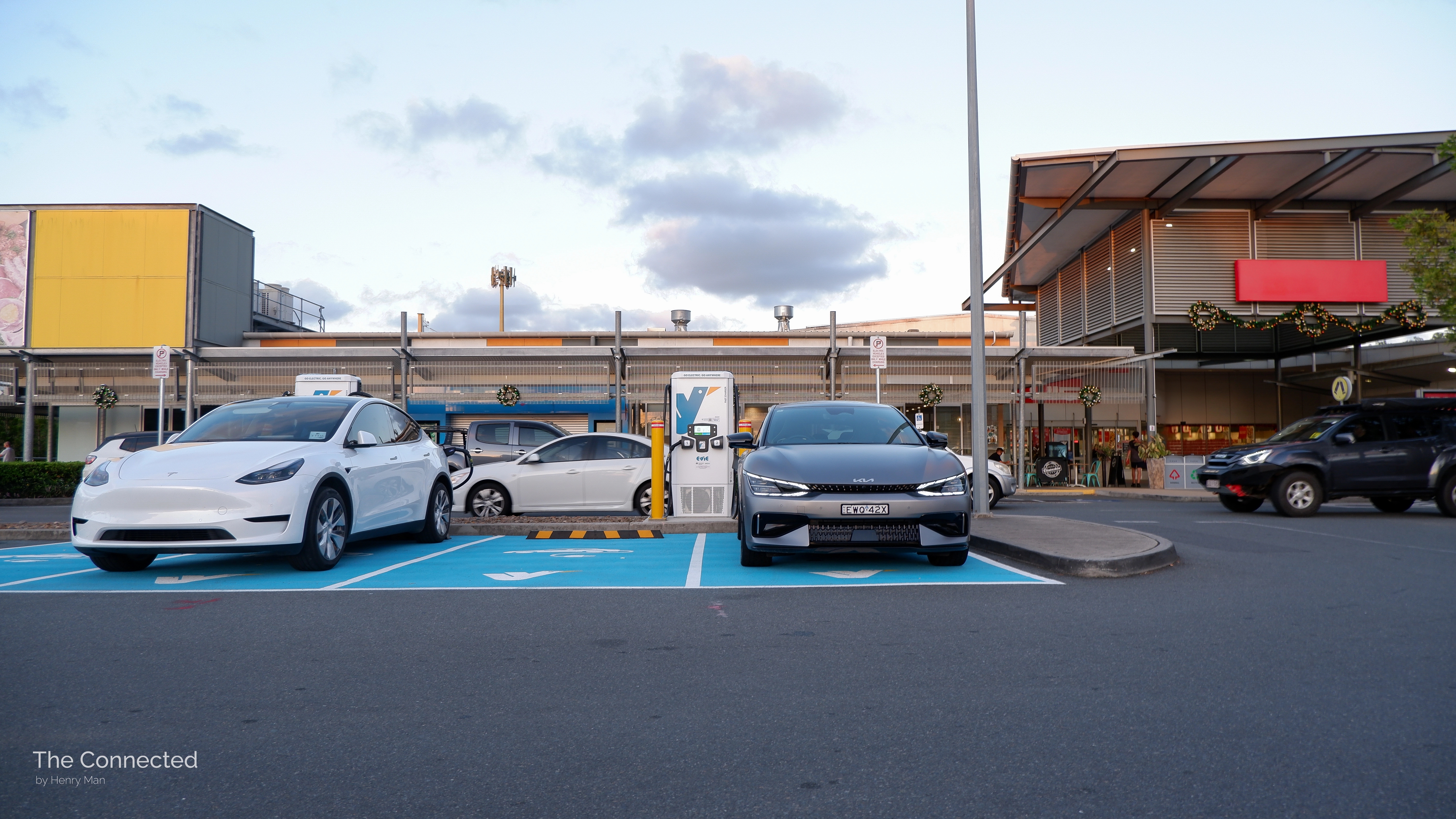 Kia EV6 and Tesla Model Y at charging station in front of shopping mall