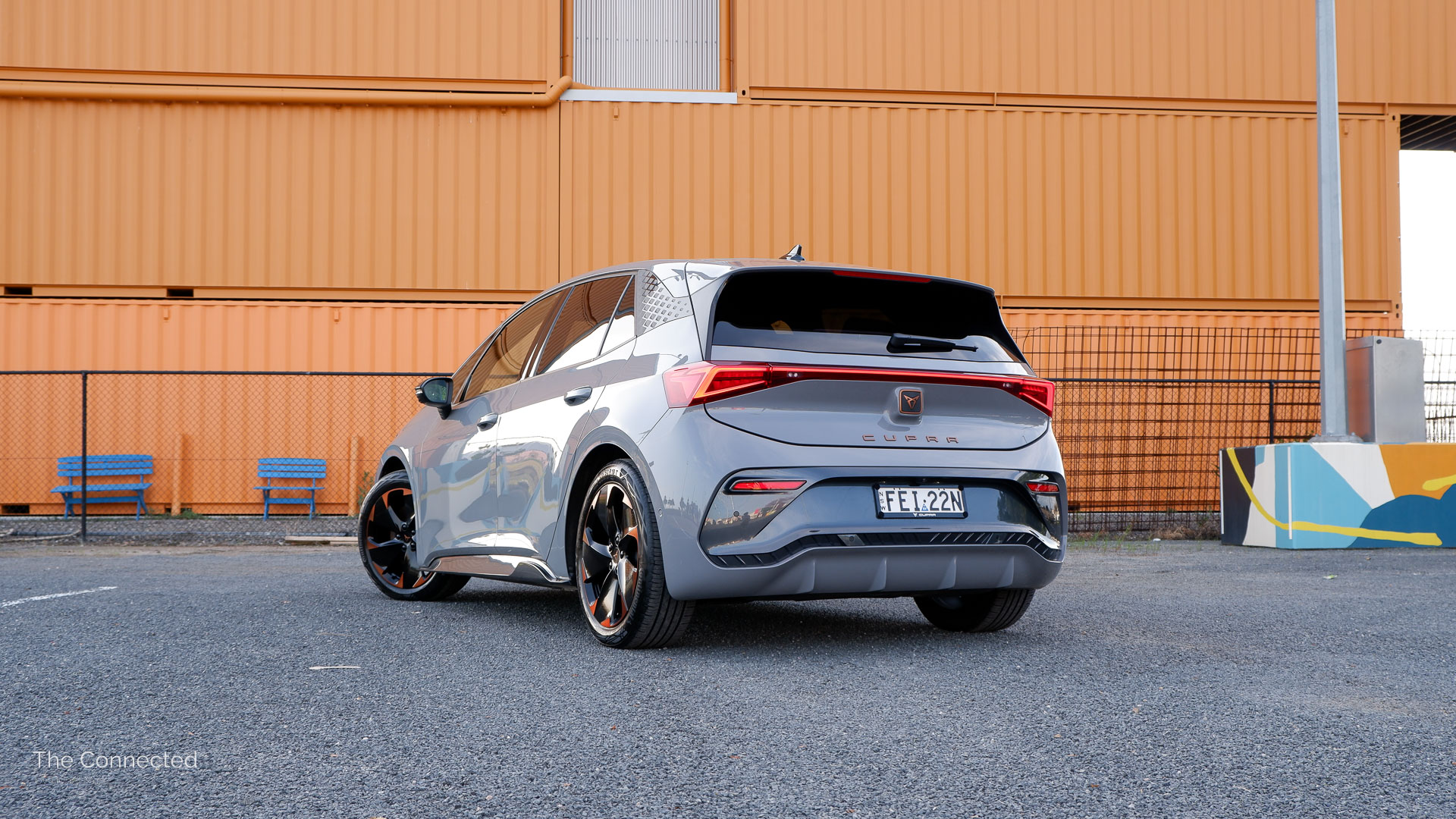 2024 Cupra Born rear three-quarter view in front of orange shipping containers