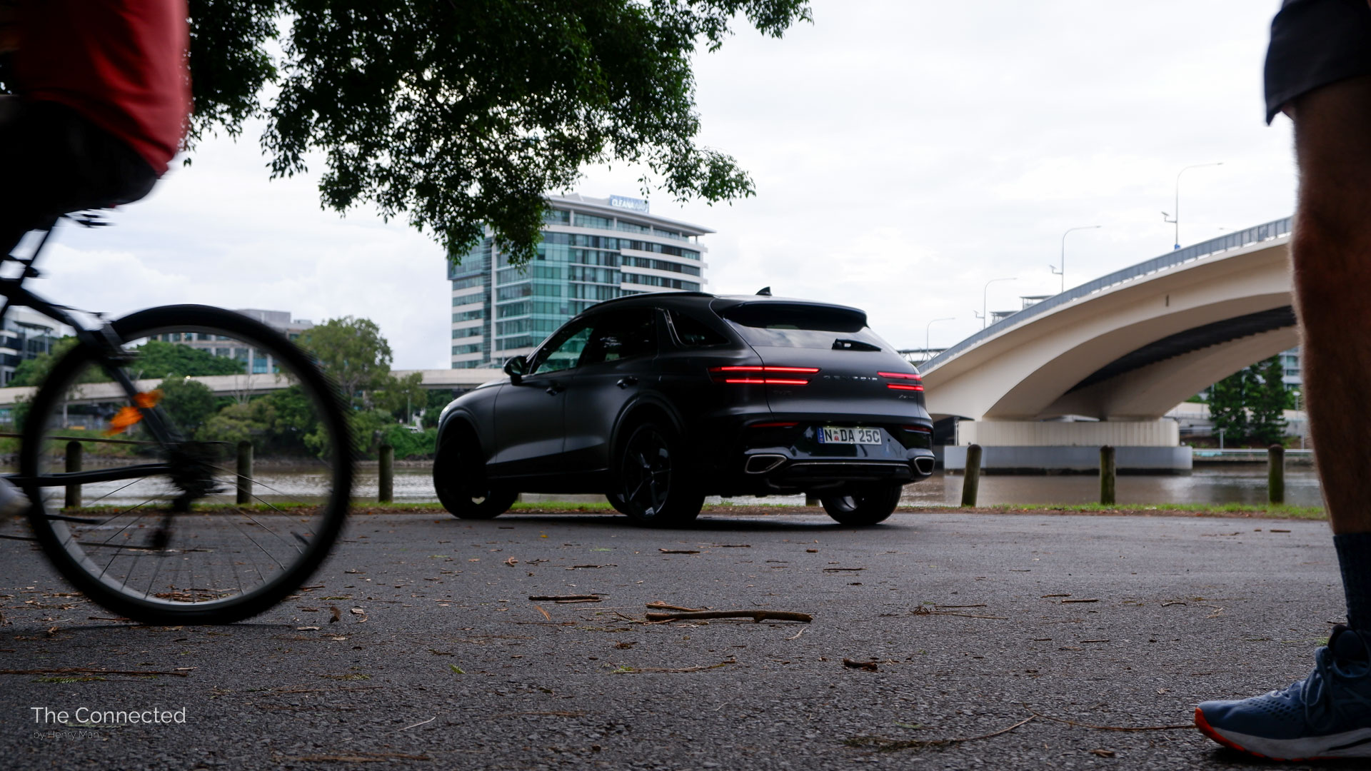 Cyclist and pedestrian move past 2025 Genesis GV70 Signature Sport rear-quarter view