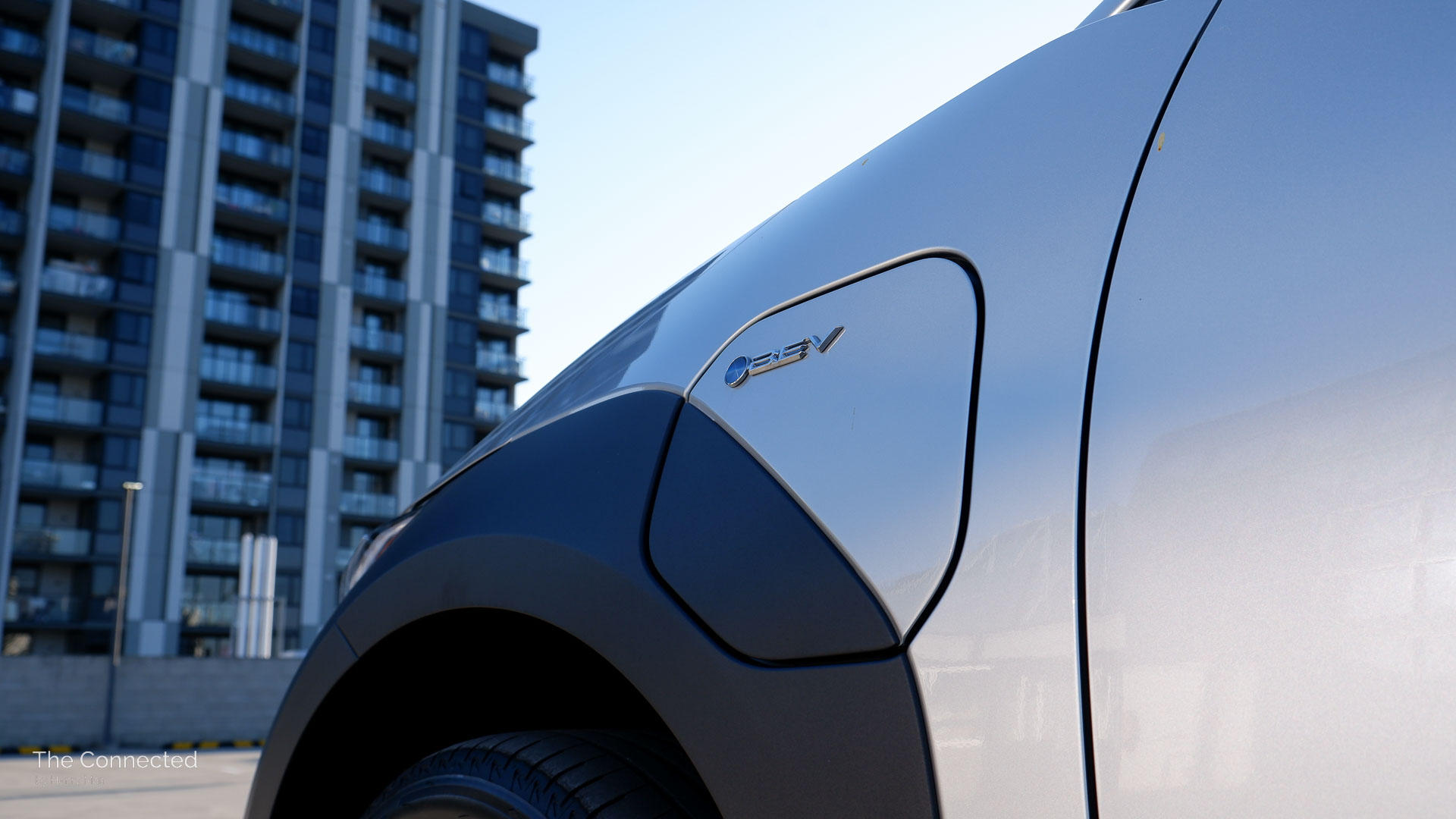 2025 Toyota bZ4X 2WD charge port with BEV logo in front of city apartment
