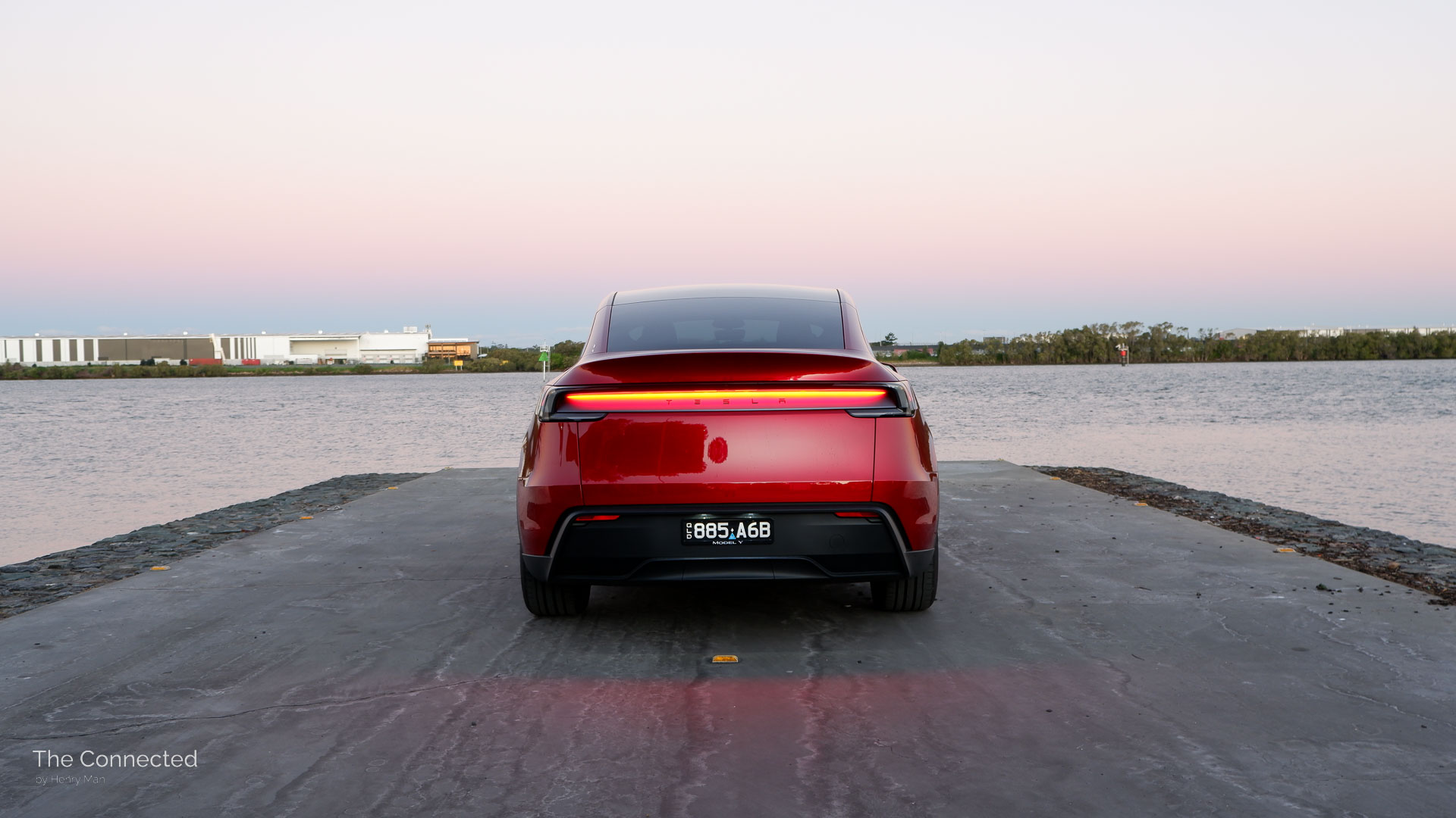 2026 Tesla Model Y RWD Ultra Red rear view in sunset with glowing reflective tail-light bar