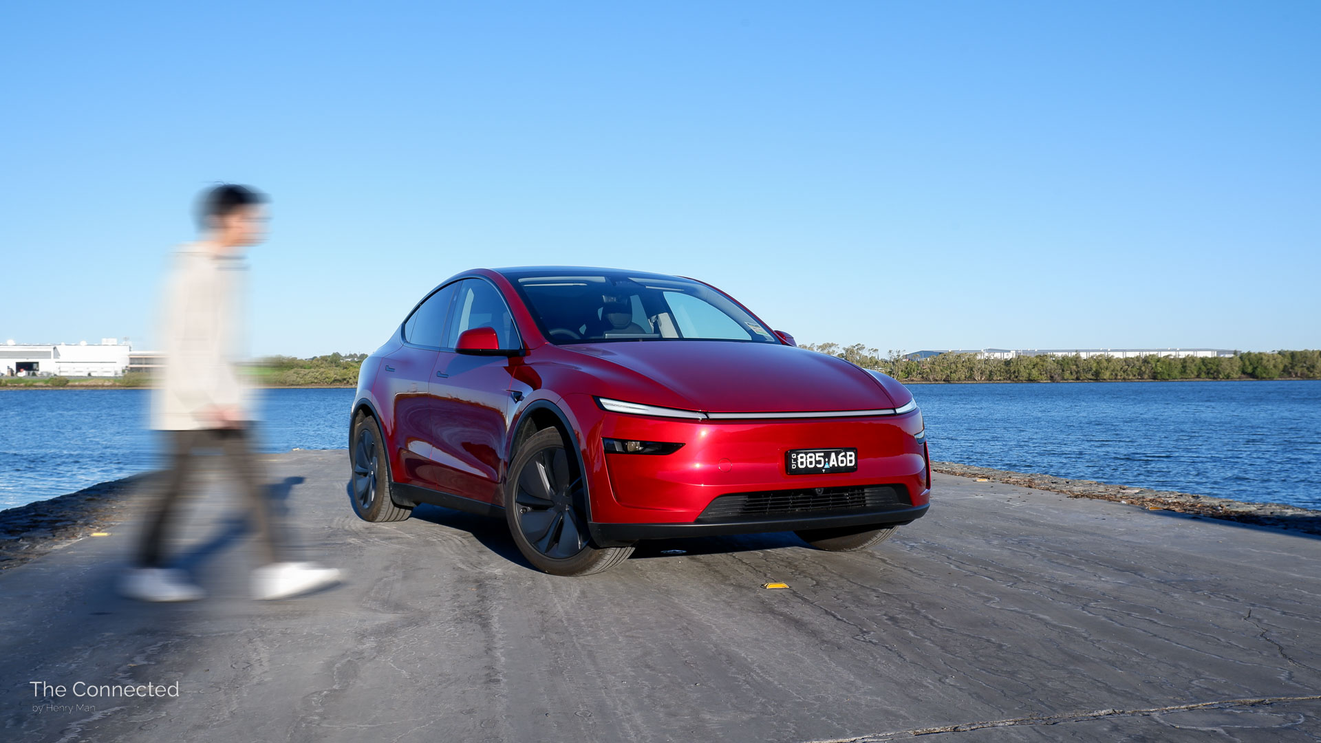 Man walks past 2026 Tesla Model Y RWD Ultra Red with the river behind