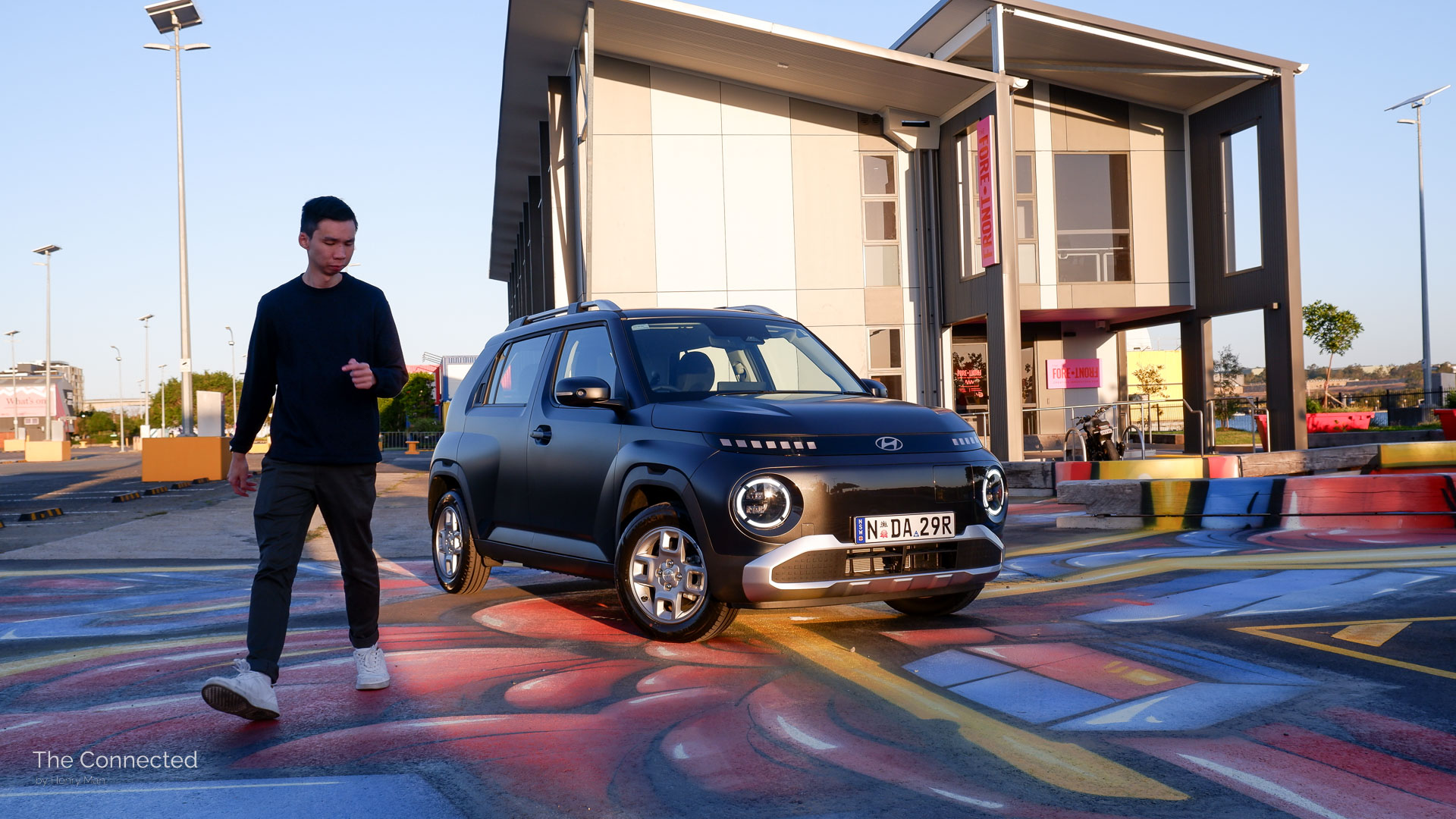 Man walks away from 2026 Hyundai Inster Standard Range with office behind and ground artwork