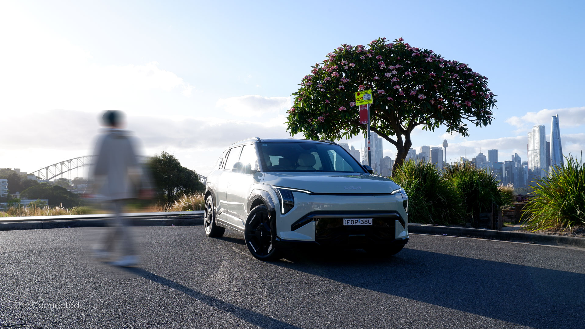 Man walks past the 2025 Kia EV3 GT-Line with the Sydney Harbour Bridge and cityscape behind