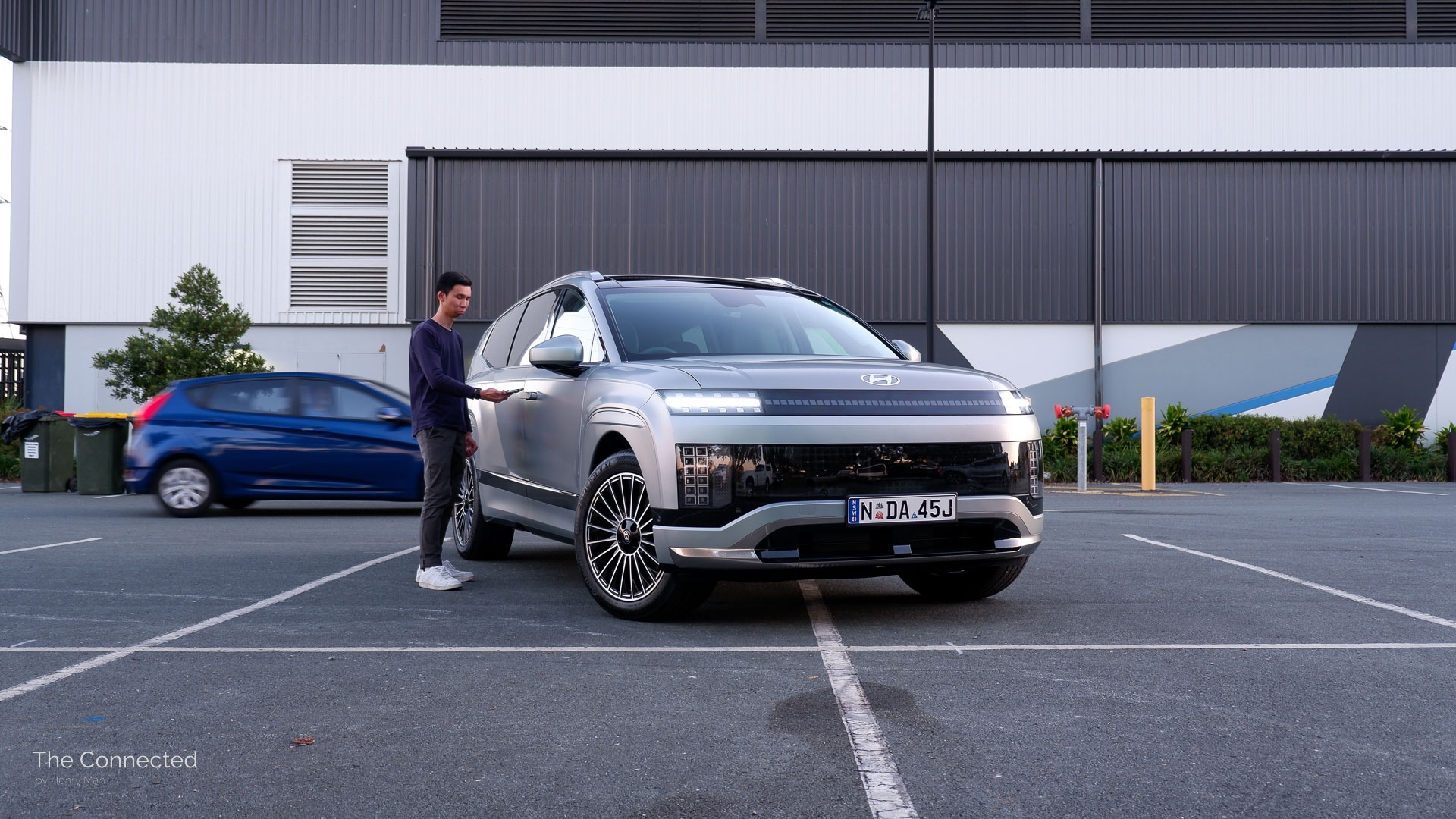 Man taps phone on 2026 Hyundai Ioniq 9 Calligraphy door handle as a blue Accent passes in the background