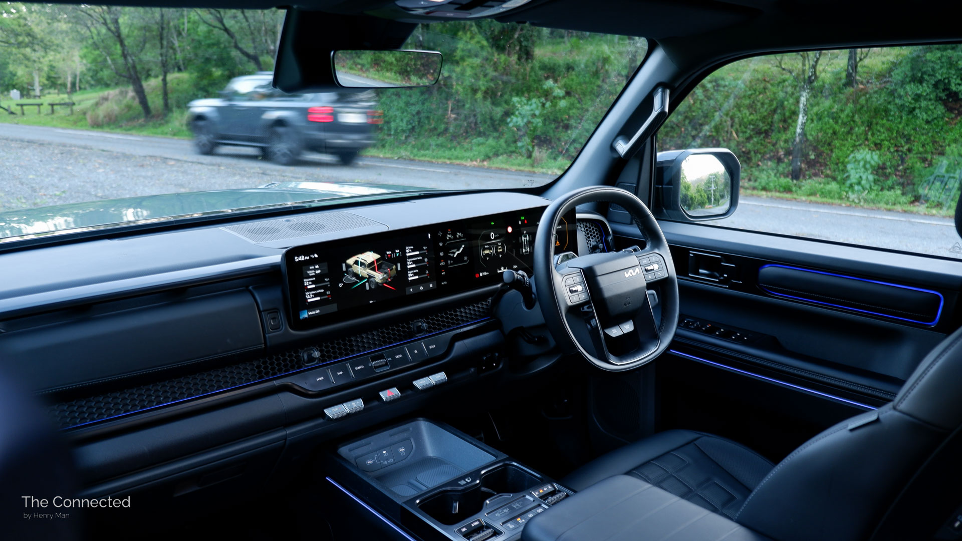 2026 Kia Tasman X-Pro interior and dashboard view with LandCruiser Prado passing in the background