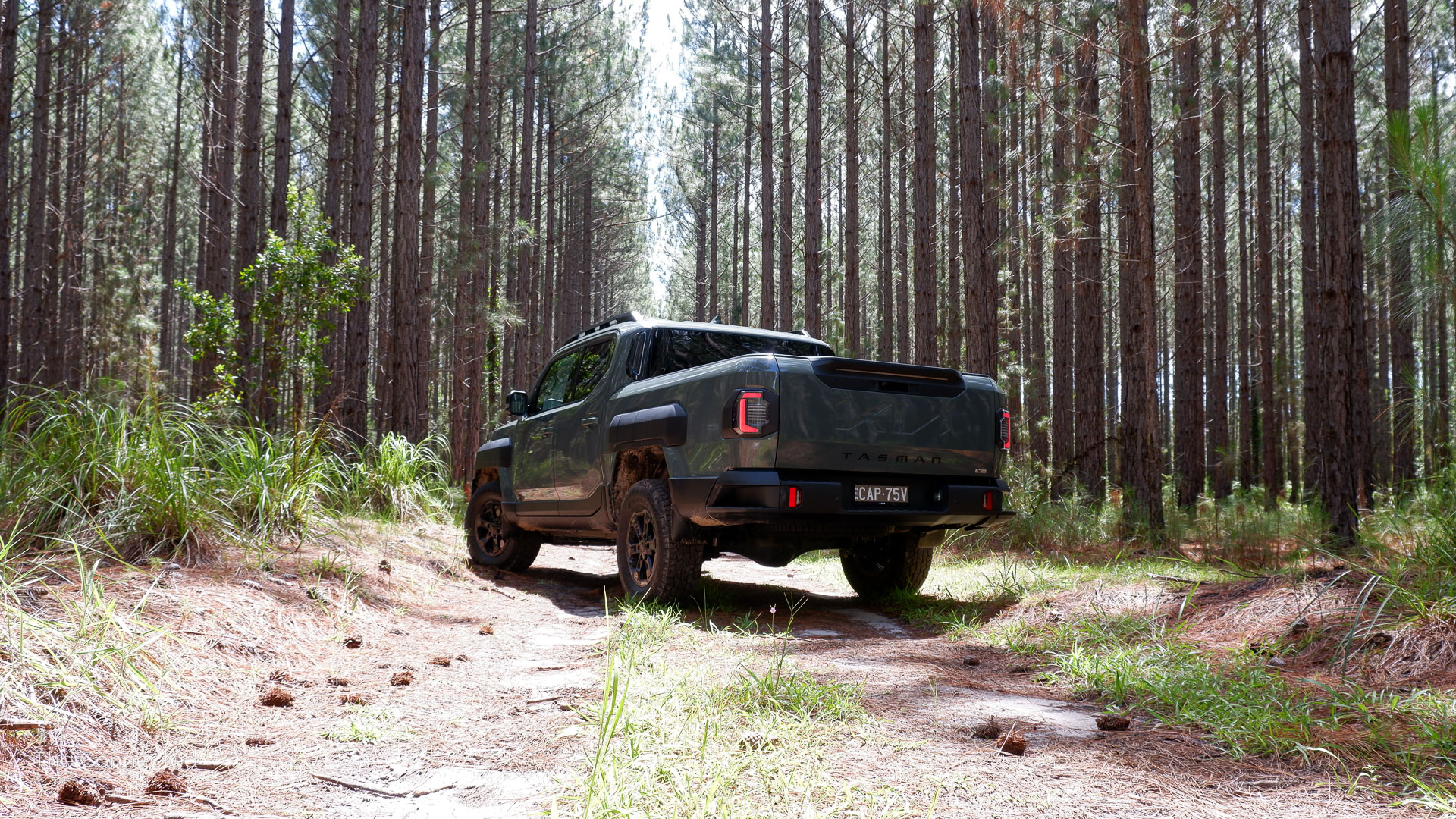 2026 Kia Tasman X-Pro rear-quarter view with forest behind