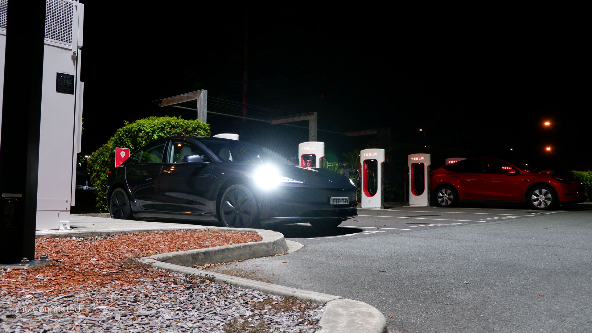 2026 Tesla Model 3 Premium Long Range RWD at a Tesla Supercharger during the night with headlights on