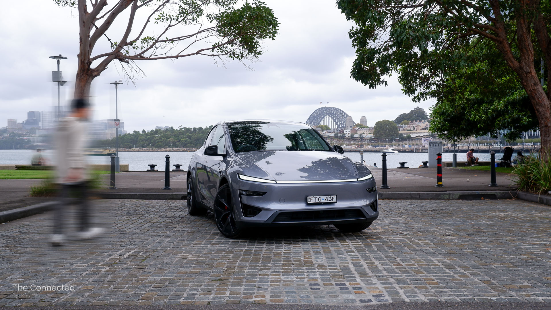 Man walks past the 2026 Tesla Model Y Performance with Sydney Harbour Bridge and riverfront in the background