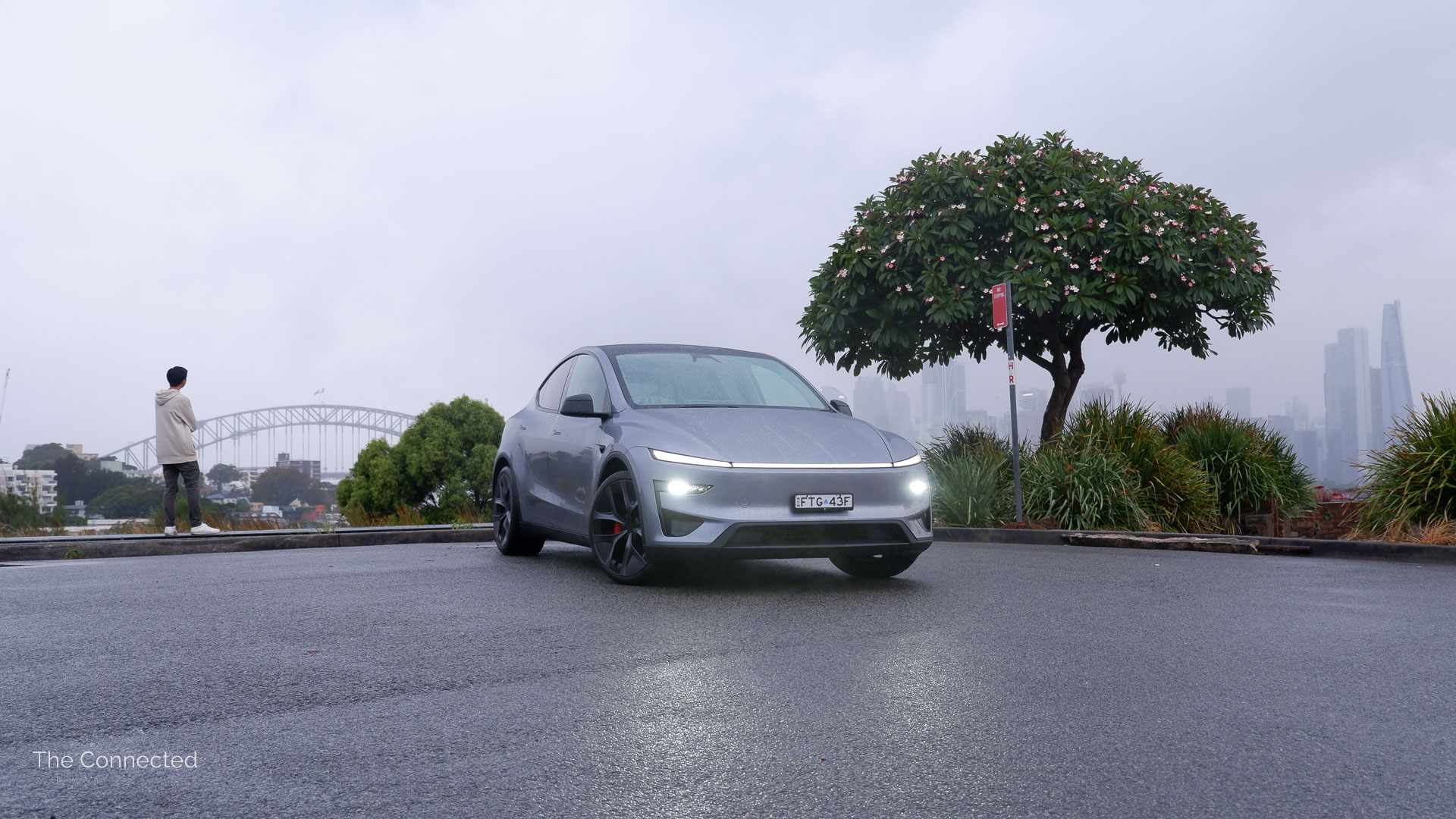 Man looking at the Sydney Harbour Bridge beside the 2026 Tesla Model Y Performance AWD