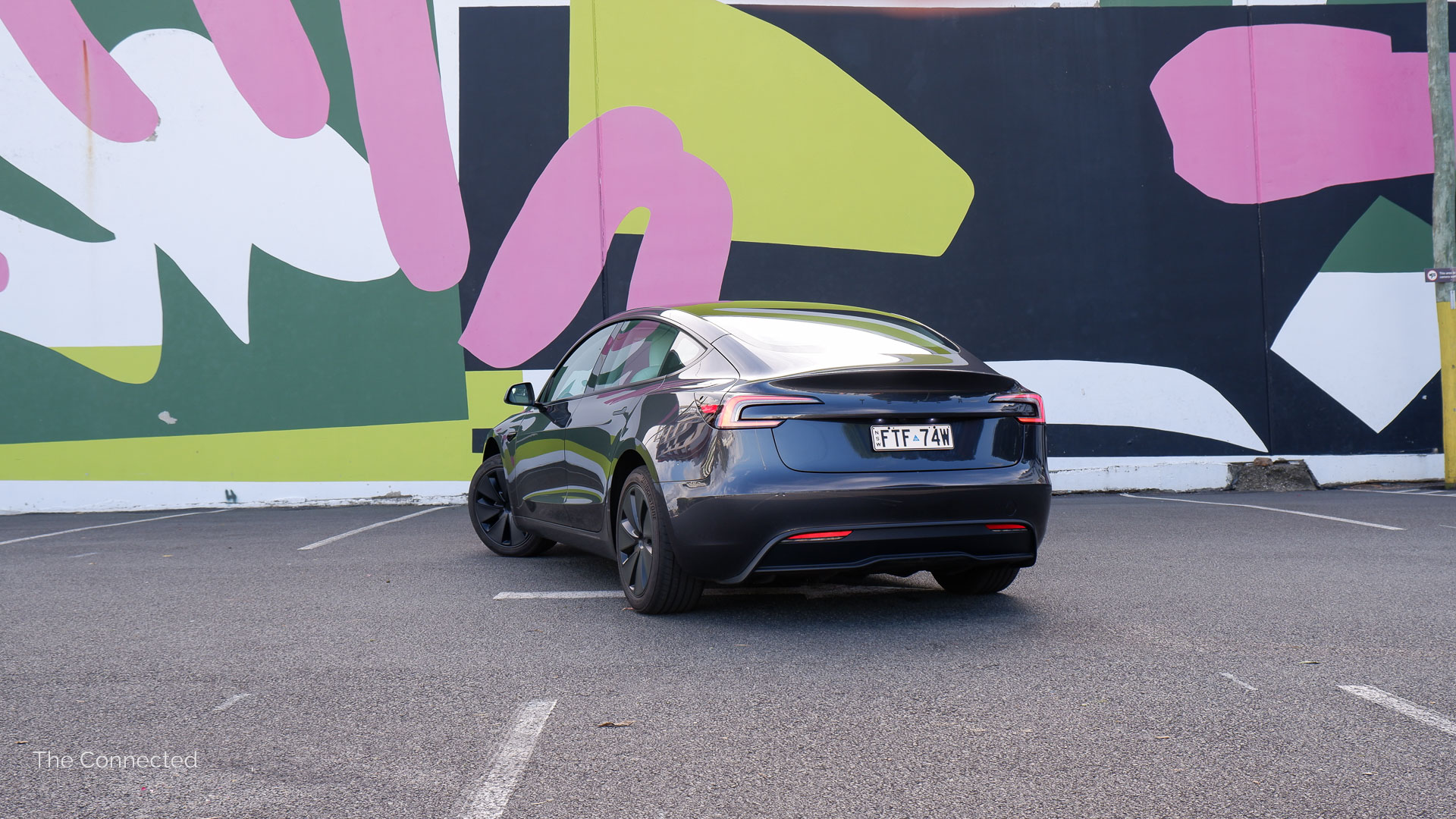 2026 Tesla Model 3 Premium Long Range RWD rear-quarter view with an artwork wall behind