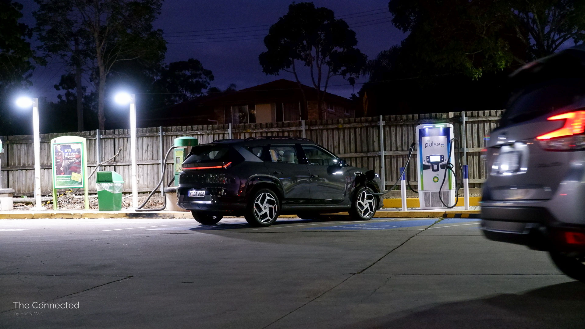 2026 Hyundai Elexio Elite charging at public DC charging station during the night while a car passes